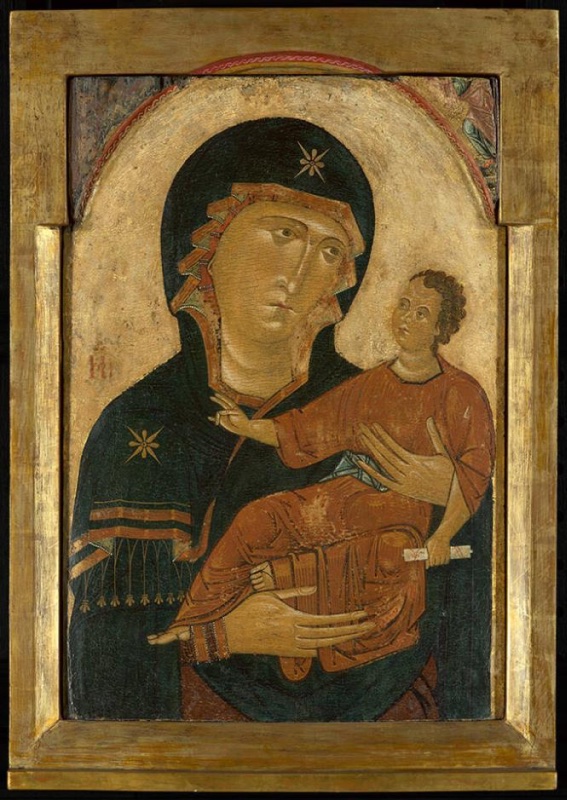 Arched gold-ground panel in a plain gilded frame. The Virgin, in a dark blue-green mantle with gold stars on her forehead and shoulder and a fringed, striped border, holds the Christ Child on her left arm. The Child, in an orange-red robe, raises his right hand in blessing and holds a small white scroll, while her long-fingered hand rests beneath him. The upper corners retain only worn fragments of painted figures