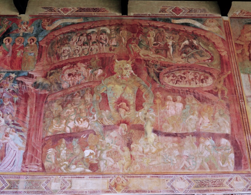 Medieval fresco of Hell by Buonamico Buffalmacco in the Camposanto of Pisa, c. 1336–41. Hell is shown as the interior of a rocky mountain divided into levels where devils torment naked sinners with serpents, fire, a boiling cauldron, and a dragon's maw. At the centre a gigantic horned, tusked Lucifer chews one sinner while another emerges from a second face at his belly. At the left, haloed apostles and angels with the Cross preside as crowned and mitred figures among the damned are driven toward the abyss. Painted scrolls with inscriptions label the sins and punishments.