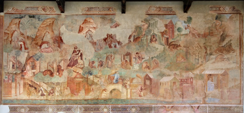 Large medieval fresco of the Thebaid by Buonamico Buffalmacco in the Camposanto of Pisa, c. 1336–41, showing the desert of the Egyptian hermits as a rocky landscape with palms and small chapels. Dozens of episodes from the lives of the Desert Fathers appear across the mountain: Mary of Egypt, covered by her own hair, kneels before the monk Zosimas; lions recall the legend of Paul the Hermit; a hermit at upper right confronts a winged demon; other monks weave baskets, dig, read, and pray. Along the bottom the Nile, full of fish, separates the desert from a walled city, with a camel driver, a fisherman, and a rider crossing a bridge. Areas of bare plaster mark losses from the 1944 fire.