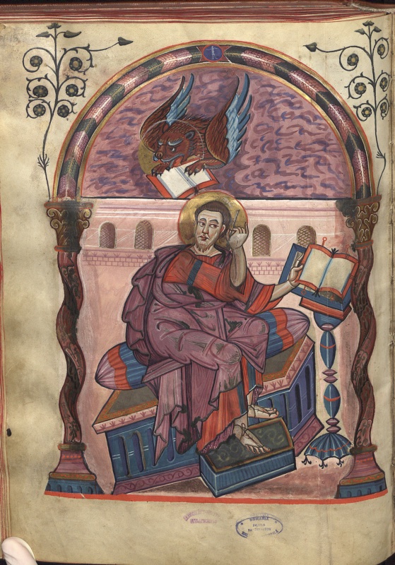 Evangelist portrait from the Codex Aureus of Lorsch: Saint Mark in a purple mantle seated on a cushioned throne, turning with pen raised beside his ear toward an open book on a tall lectern, while above him under a feathered arch his symbol, a gold-haloed winged lion, plunges through a violet sky clasping an open book