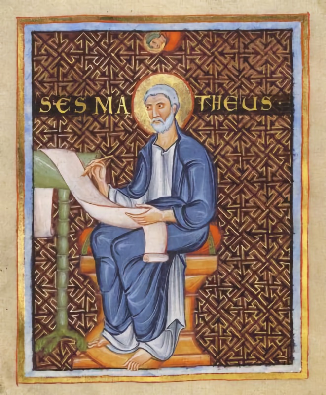 Full-page medieval miniature framed in blue and gold: an elderly white-bearded saint with a gold halo, in a white tunic and deep blue mantle, sits barefoot on a block-like seat with a red cushion, writing with a pen on a long scroll that runs from a green-columned lectern across his lap; the background is purple covered with a dense gold geometric pattern, gold letters across it give his name, and a small haloed half-figure looks down from a roundel at the top
