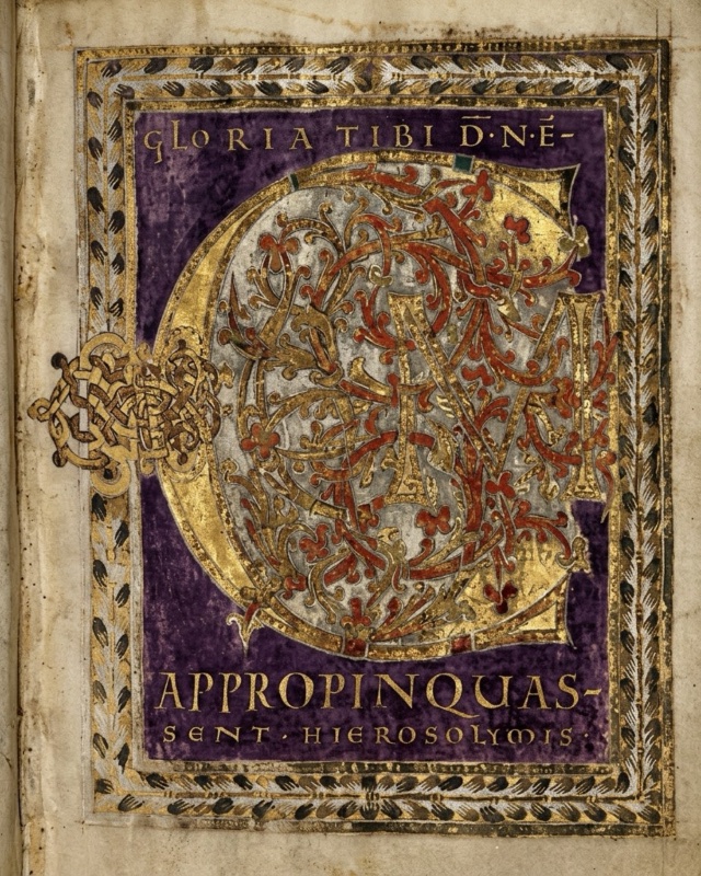 Medieval manuscript page with a deep purple field framed by a border of dark leaves and gold: almost the whole field is filled by a large gold letter C whose interior is silver, covered with a dense web of gold and vermilion interlace and scrolling stems with trefoil leaves, with the gold letters U and M woven into it; a knot of plaited gold interlace projects into the left margin; a line of gold capitals above reads GLORIA TIBI DNE, and two lines below read APPROPINQUASSENT HIEROSOLYMIS