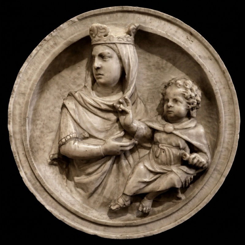 Circular marble relief within a plain raised rim, showing a crowned and veiled Virgin seated at the left with the Christ Child at the right; both figures are polished and fully carved while the ground behind them remains rough, and their feet project at the lower edge of the disc.