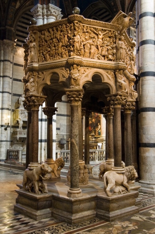 Octagonal marble pulpit raised on nine columns, four of them standing on lions devouring their prey; trilobed arches span the intervals and the parapet above is carved with densely populated relief panels separated by standing figures, with an eagle lectern projecting at the right.