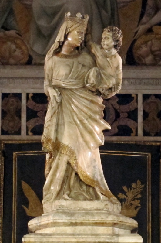 Small marble statue of a crowned and veiled Virgin standing with the Christ Child held high on her left arm; her mantle is drawn across the body in a long diagonal ending in a broad gilded and fringed hem. The Child turns his head back toward her and reaches one arm up toward her crown.