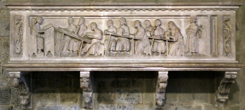 Marble sarcophagus relief from the tomb of Cino da Pistoia, attributed to Agostino di Giovanni, 1337–1339: the jurist lectures from a tall lectern at left while nine students follow at sloped desks — listening, writing, conferring and reading — and a figure stands at the school door at right; Pistoia Cathedral