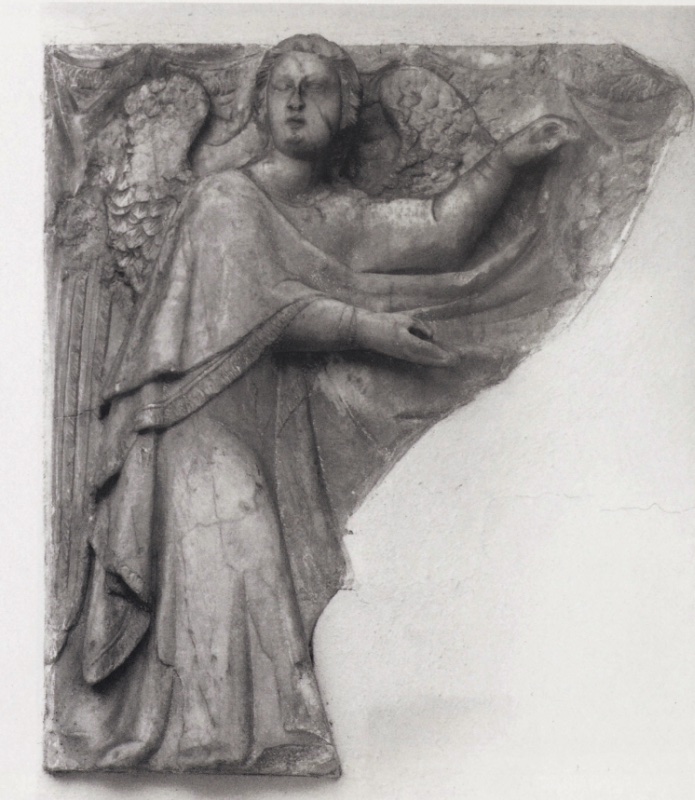 Fragmentary marble relief attributed to Giovanni di Agostino, c. 1331: a winged angel with a soft oval face and downcast eyes, mantle bordered by an embroidered hem, raises one hand high and lowers the other over the surviving folds of a curtain whose swags hang from the top edge; the slab is broken diagonally where the curtain and the saint's effigy once continued; Museo Diocesano d'Arte Sacra, Volterra.