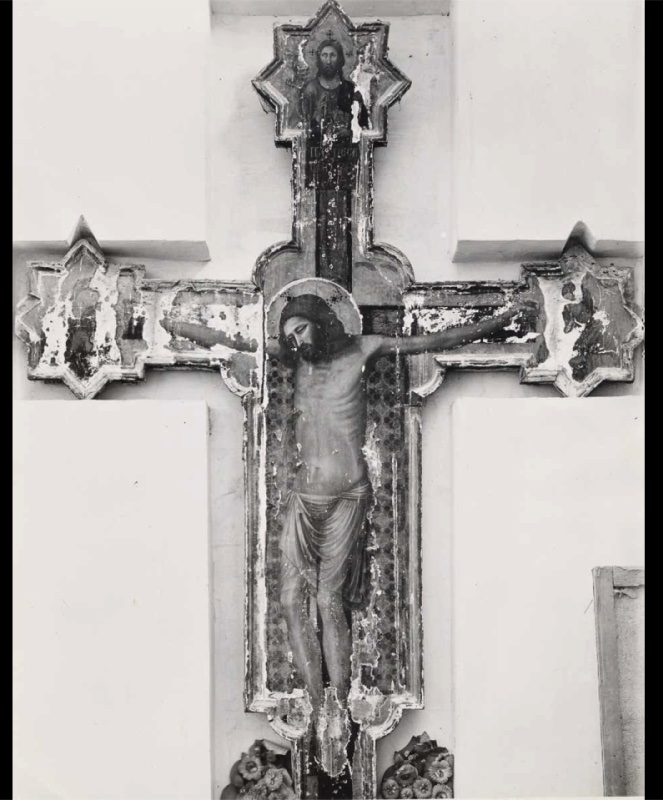 Painted cross in the church of San Francesco at Sassoferrato, c. 1310–1320, tempera and gold on panel, shown in a black-and-white archival photograph: the dead Christ hangs against an apron decorated with a rosette-patterned textile, head fallen to his right shoulder within a large punched halo; the shaped cross has eight-lobed star terminals, with a blessing figure at the summit and abraded mourning figures at the ends of the arms; the paint surface shows extensive flaking losses