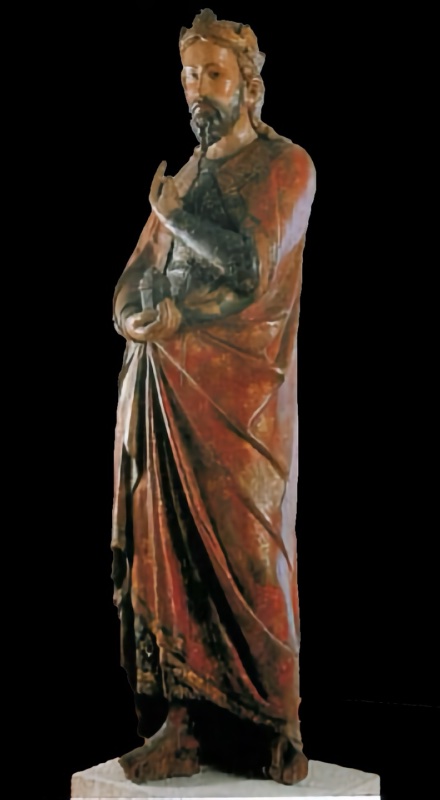 Fourteenth-century life-size painted wooden statue of a crowned, bearded Magus standing in a red mantle over a darkened blue tunic with traces of gilding; his right hand holds a small covered vessel and his raised left index finger points upward to the star. Maestro dei Magi di Fabriano, Pinacoteca Civica Bruno Molajoli, Fabriano.
