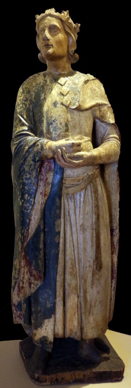 Fourteenth-century life-size painted wooden statue of a young, beardless, crowned Magus standing with head turned and raised, holding an open gift vessel in both hands; traces of blue mantle with red lining survive over a pale tunic and dagged shoulder-cape. Maestro dei Magi di Fabriano, Museo Nazionale del Palazzo di Venezia, Rome.