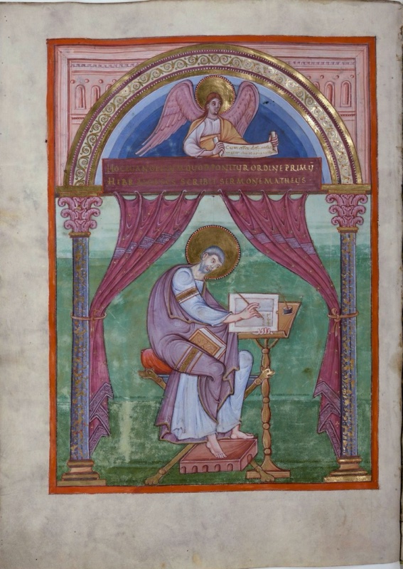 Ottonian manuscript miniature framed by an arch on two marbled columns with pink foliate capitals, set against a pink wall with blind arcades. In the lunette, a haloed, winged angel seen half-length against a blue ground holds an inscribed scroll. Below it a purple band carries two lines of gold capitals. Red curtains hang from the beam and are tied around the columns. Beneath them, on a green ground, the haloed, bearded evangelist Matthew sits on a folding stool with a red cushion, wearing a white tunic and a mauve mantle, a closed gold book on his lap and his bare feet on a footstool, writing in a book on a tall turned lectern with an inkhorn
