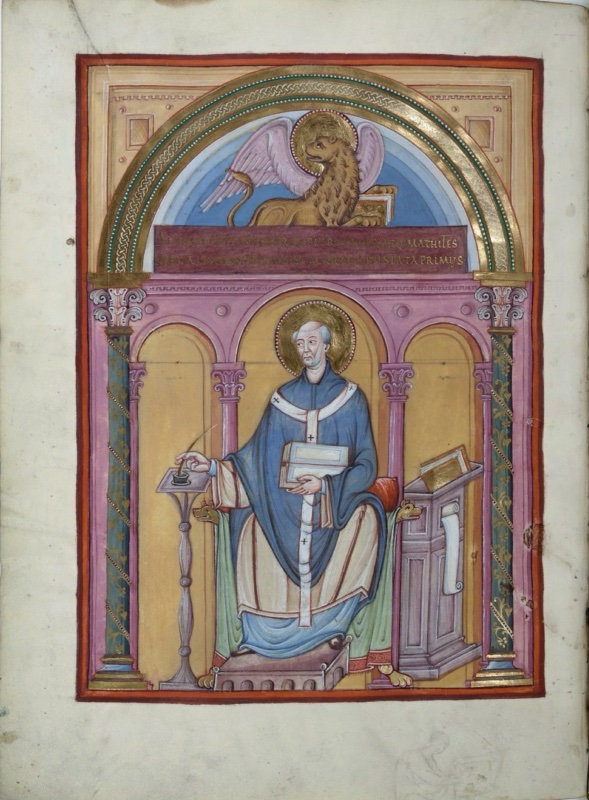 Ottonian manuscript miniature framed by a large arch on marbled green columns with gold spiral ornament. In the lunette, a haloed, winged golden lion holding a book lies on a purple band inscribed with two lines of gold capitals. Below, within a pink arcade of three arches on slender columns against an ochre ground, the haloed evangelist Mark, elderly and grey-haired, sits frontally on a throne with animal-head arms and lion-paw feet. He wears a blue chasuble and a white pallium marked with black crosses, holds a closed book, and dips a quill into an inkwell on a slender turned stand at left. At right stands a tall cabinet lectern with books and a hanging scroll. A faint sketch of a seated figure is visible in the lower margin