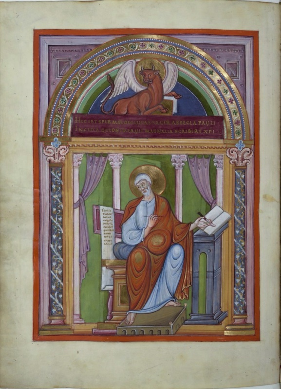 Ottonian manuscript miniature framed by an arch on marbled columns with white vine tendrils and pink foliate capitals. In the lunette, a haloed, winged, horned ox in reddish brown reclines on a purple band inscribed with two lines of gold capitals, its forelegs on a closed book. Below, between drawn mauve curtains and slender white columns on a green ground, the haloed evangelist Luke, with white hair and beard, sits on a gold block throne. He wears a light blue tunic and an orange-red mantle with a circular fold over his belly, holds a pen in one hand, and reaches with the other to an open book on a grey pedestal lectern. Behind him at left, a tall stand holds a book showing the opening lines of his Gospel. His bare feet rest on an arcaded footstool