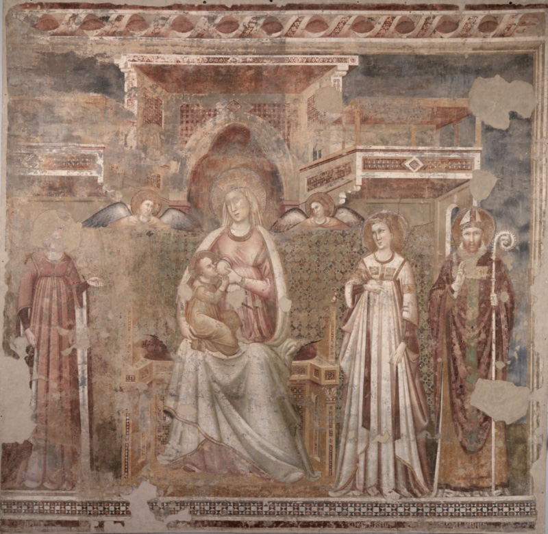 Detached fresco: the Virgin, enthroned beneath a painted canopy with a pointed arch, nurses the Christ Child; two angels hold a patterned cloth of honour behind her. To the left stands Saint Lucy, her face lost to damage; to the right, Saint Catherine of Alexandria in a pleated gown and a mitred bishop saint with crozier raised in blessing. Painted balconies with geometric marble inlay recede on either side; areas of bare plaster mark old losses.