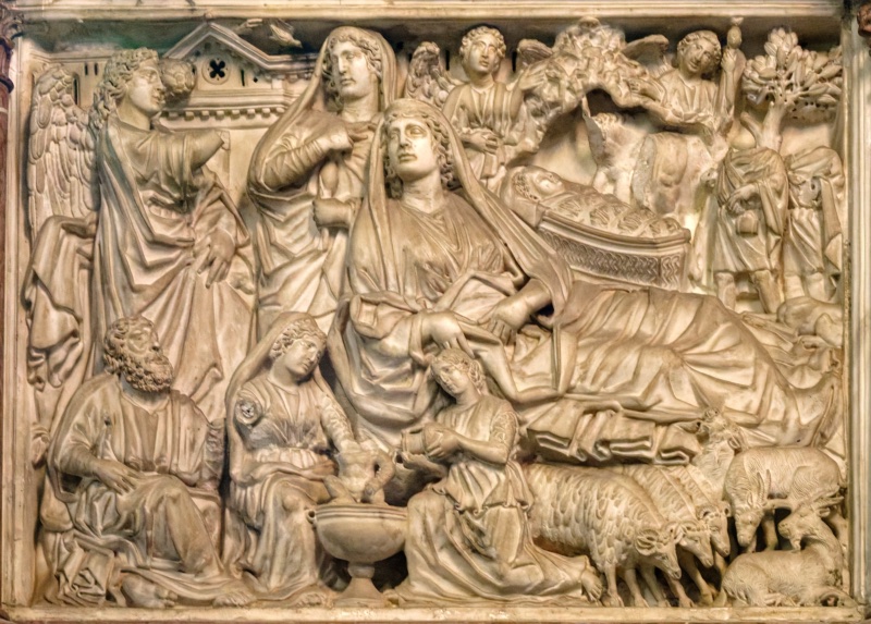 Densely carved marble relief in which a veiled Virgin reclines across the centre of the field, her head raised on one hand; above and behind her the swaddled Child lies in a manger with the ox and ass, angels and a shepherd appear at the right among trees, two women bathe an infant in a basin at the lower centre, a bearded Joseph sits in thought at the lower left, and sheep and goats fill the lower right corner.