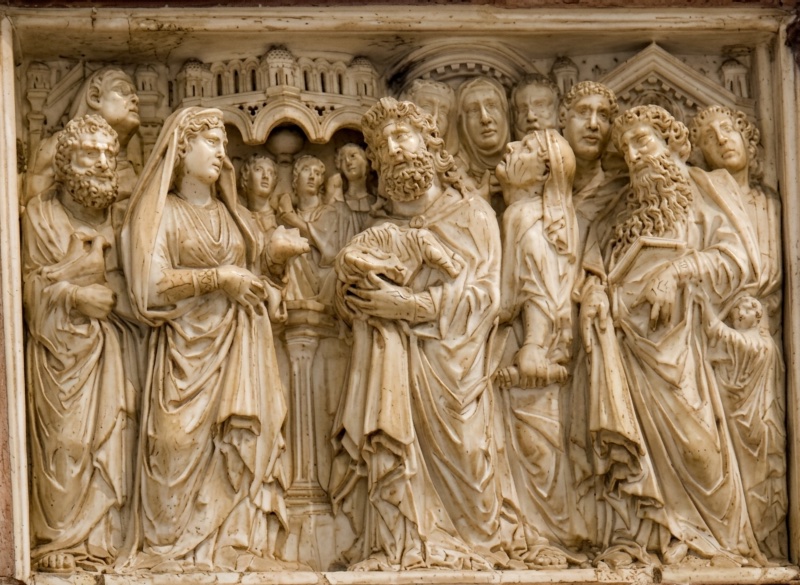 Crowded marble relief before an architectural skyline of arcades and gables: at the left a veiled woman advances with one hand raised; at the centre a slender column supports an altar; to the right a bearded elder holds a swaddled infant against his breast, with a dense press of heads behind him and a second bearded figure at the right edge.